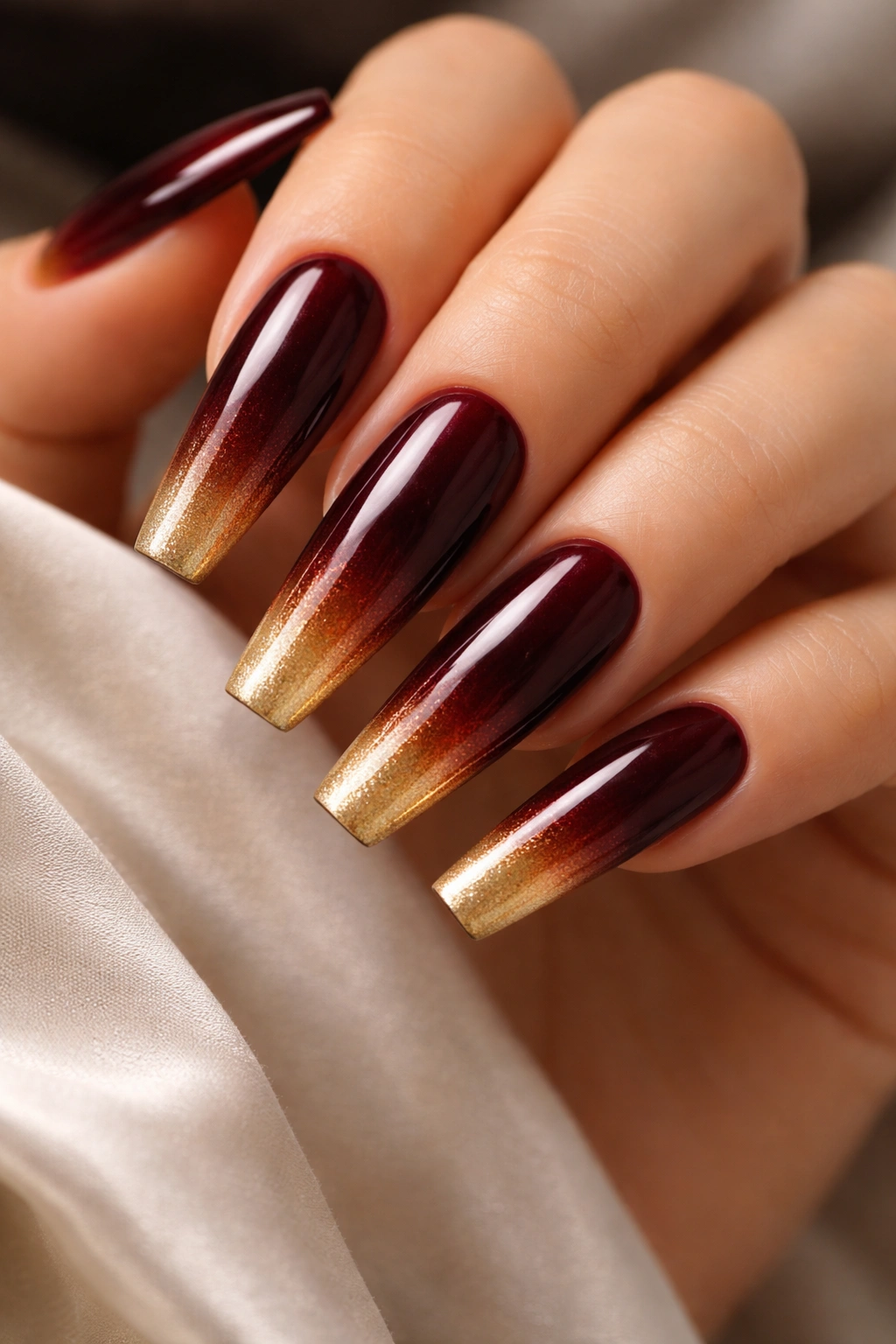 Close-up of coffin nails with burgundy to gold ombre fade on a hand