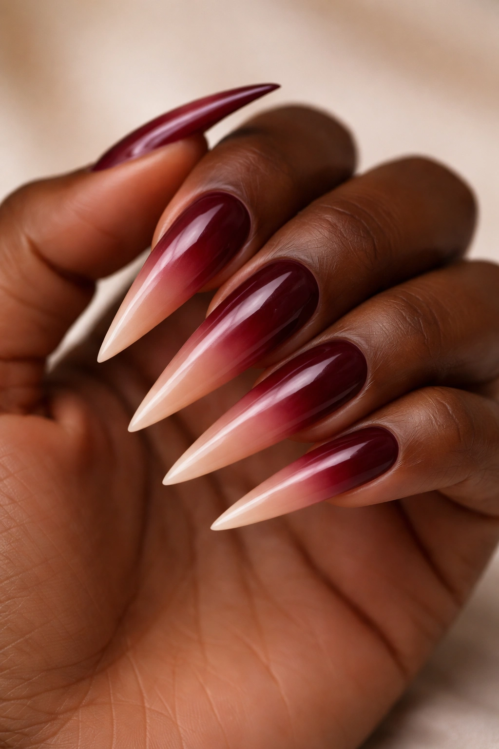 Close-up of burgundy ombre stiletto nails fading to nude on a neutral studio backdrop