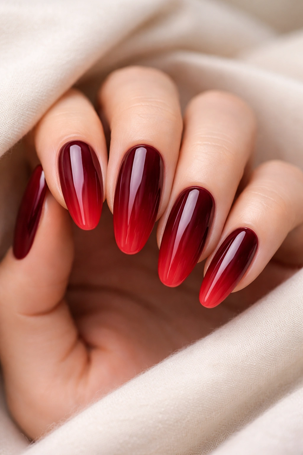 Close-up of long round acrylic nails with burgundy to red ombre gradient