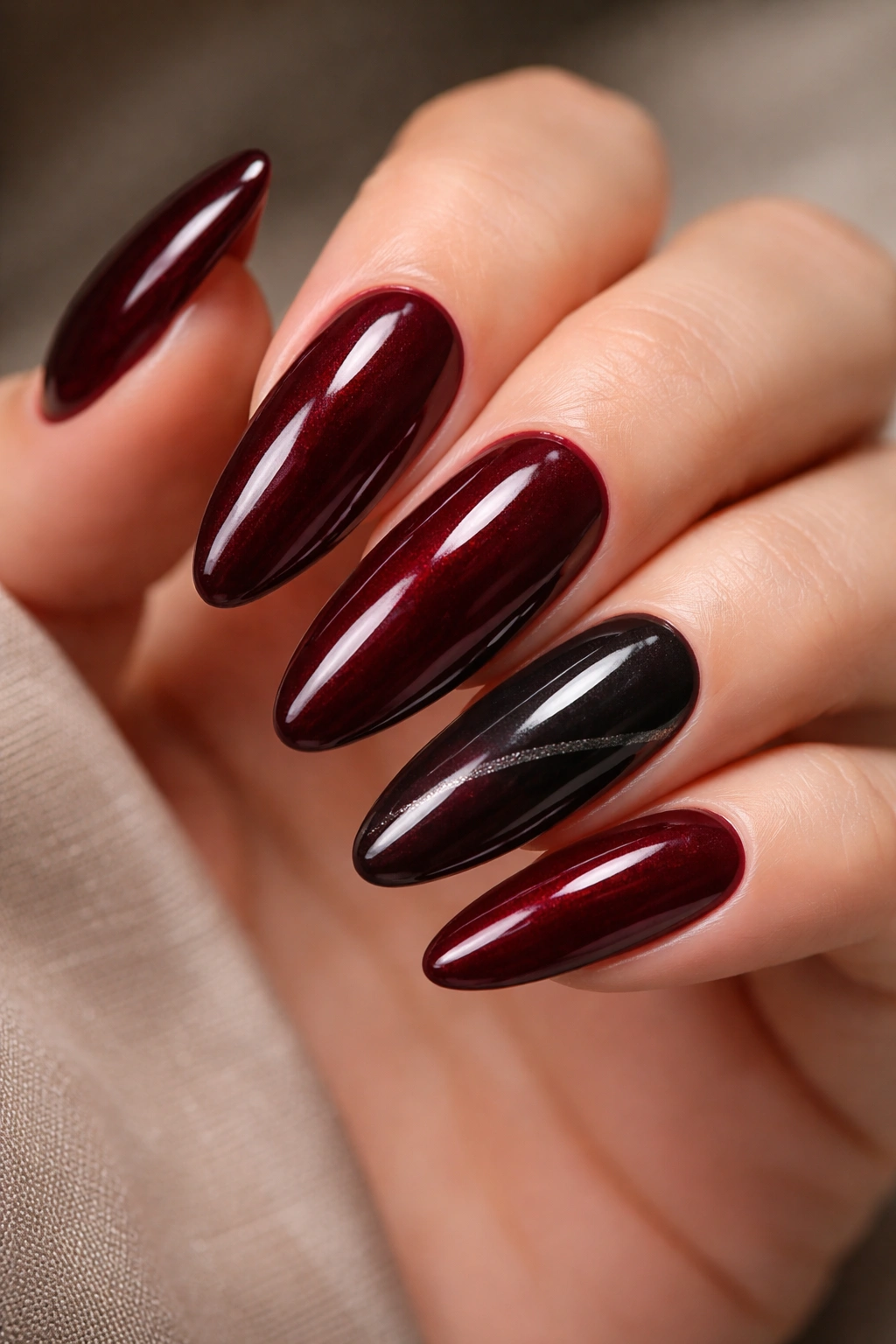 Close-up of burgundy oval nails with a sheer black accent nail and glossy finish