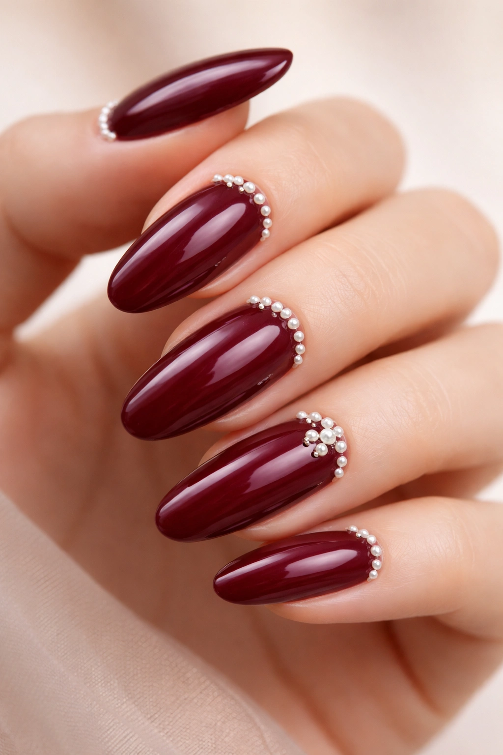 Burgundy nails with tiny pearl embellishments along the cuticle