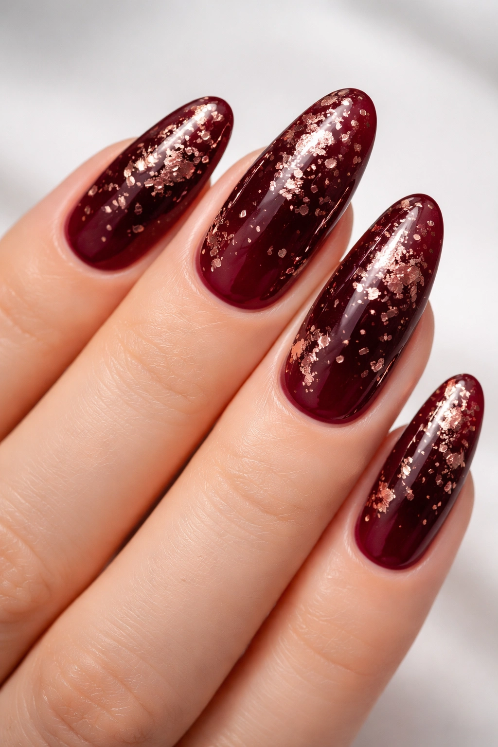 Close-up of burgundy nails with rose gold flakes on long oval nails