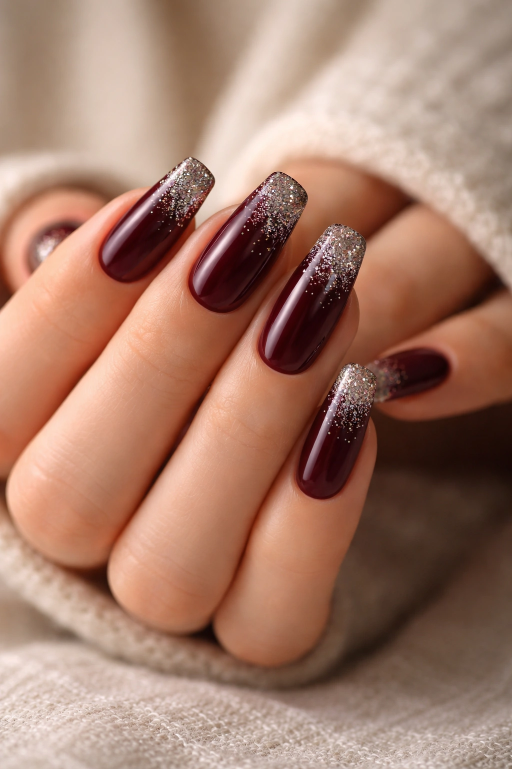 Deep burgundy coffin nails with sparkly gradient tips on a neutral background