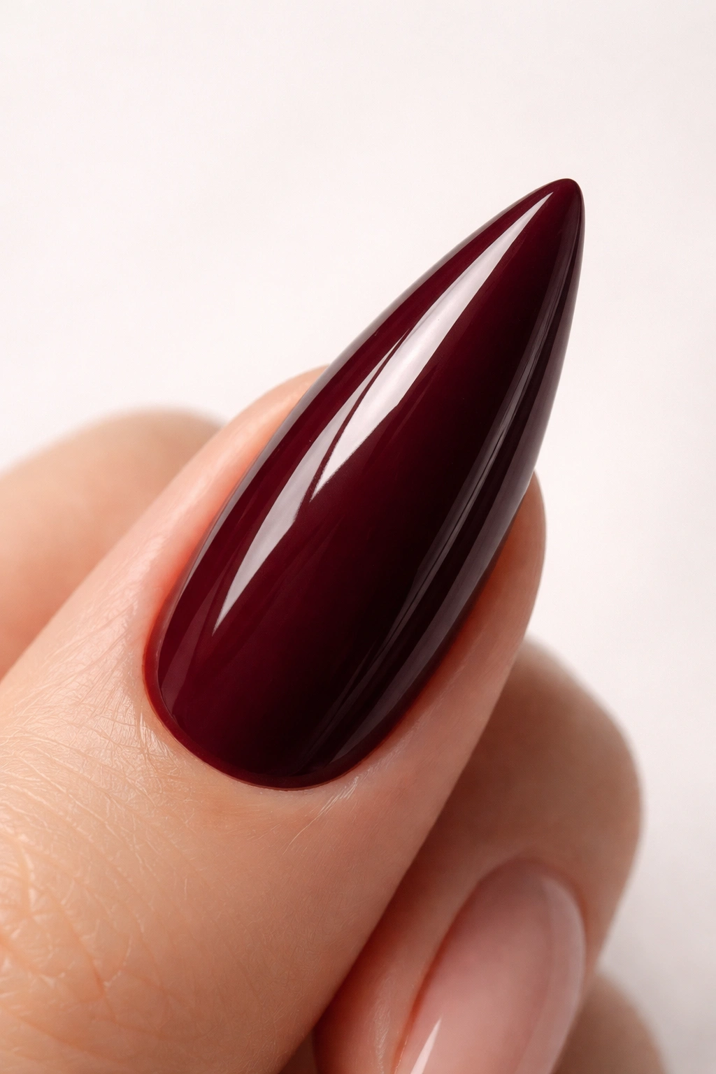 Close-up of a deep burgundy stiletto nail with a glossy topcoat on a neutral background