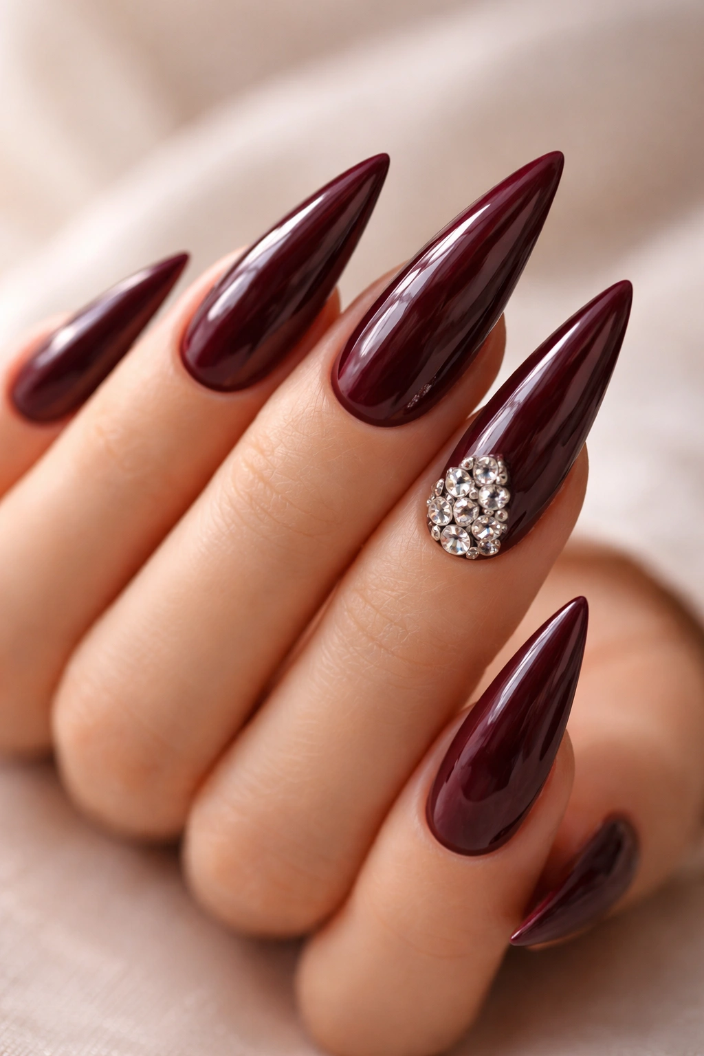 Close-up of burgundy stiletto nails with glossy finish on a neutral background
