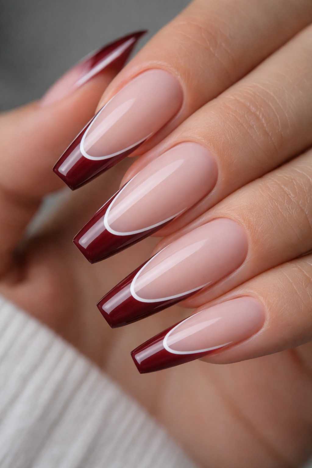 Close-up of burgundy French tips with a razor-thin white outline on long ballerina nails