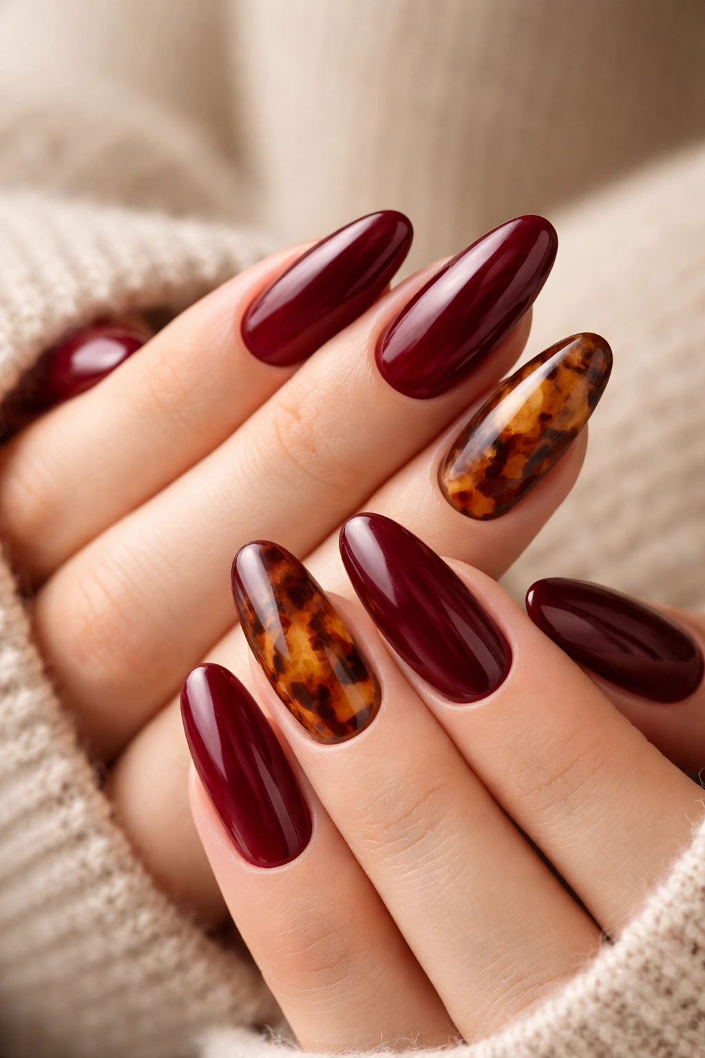 Close-up of long oval nails showing burgundy nails with tortoiseshell accents on one or two nails
