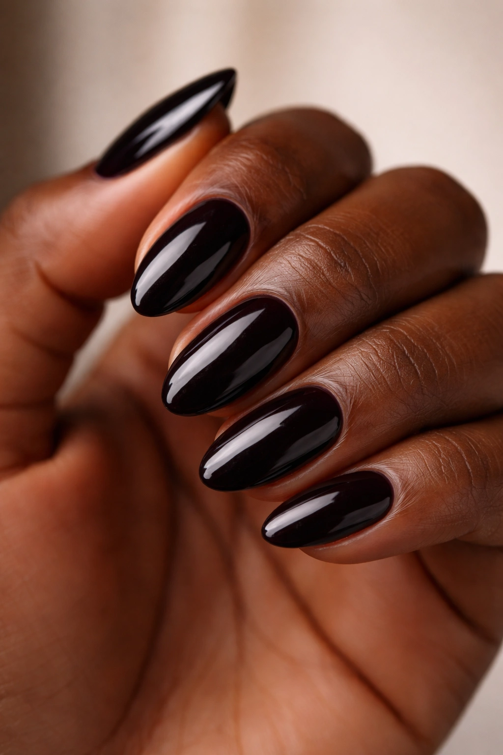 Close-up of dark-skinned hand nails in near-black burgundy-toned polish on short almond nails