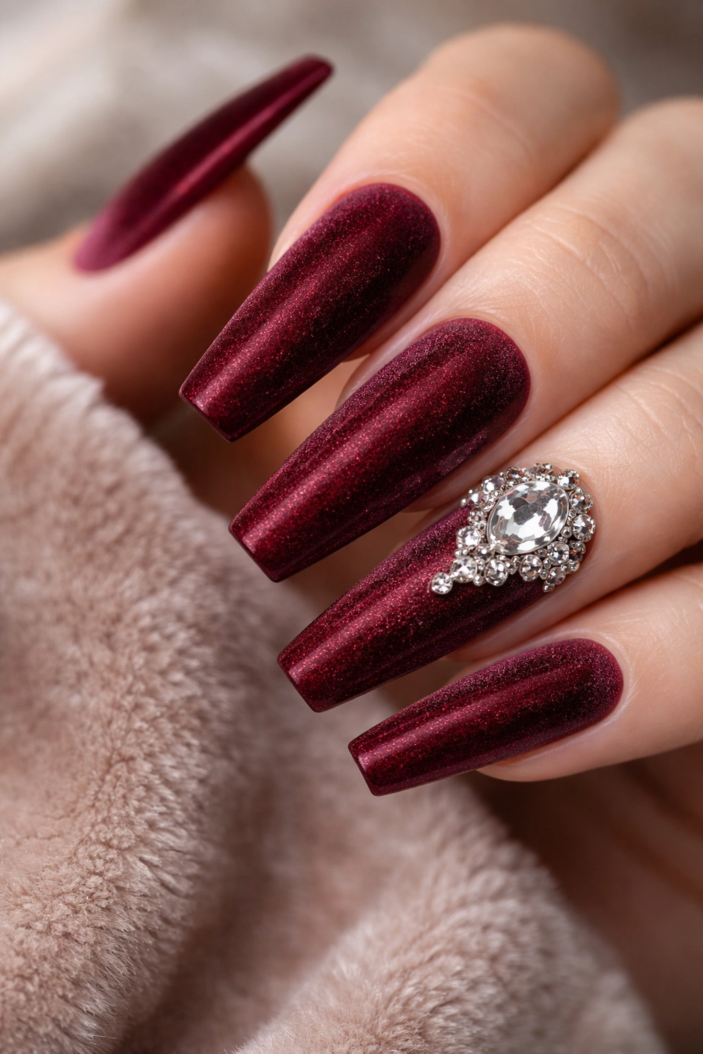 Close-up of burgundy velvet coffin nails with a clear crystal accent