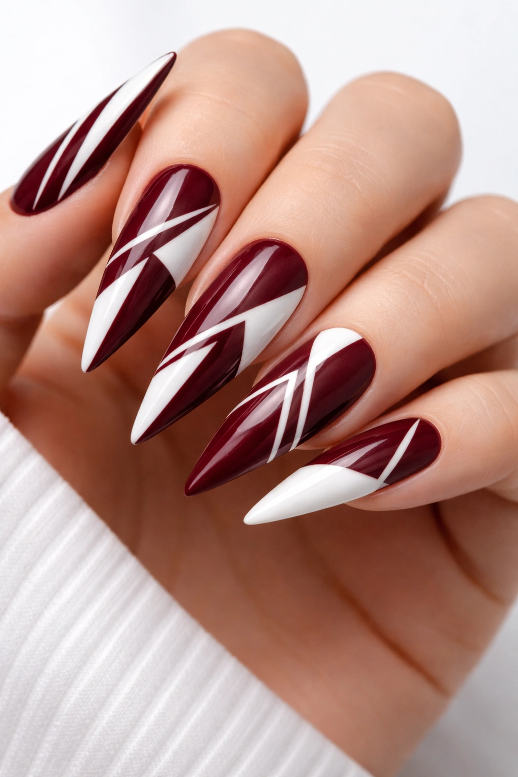 Burgundy stiletto nails with white geometric patterns.