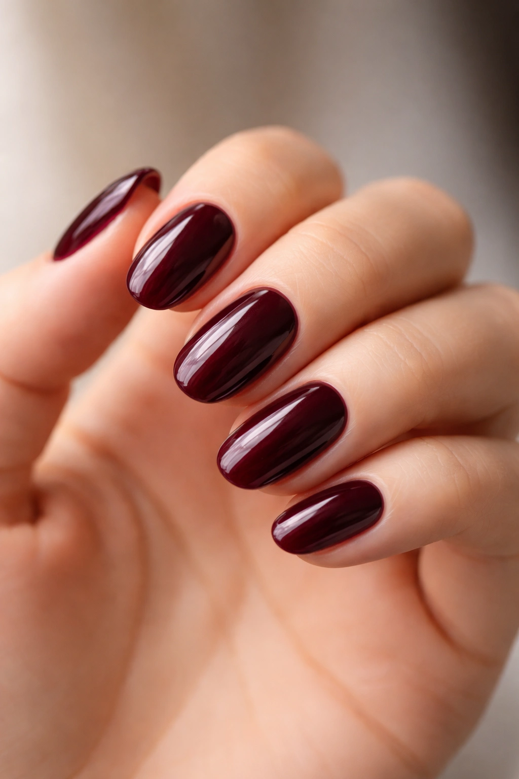 Close-up of short oval nails in deep burgundy wine with glossy shine