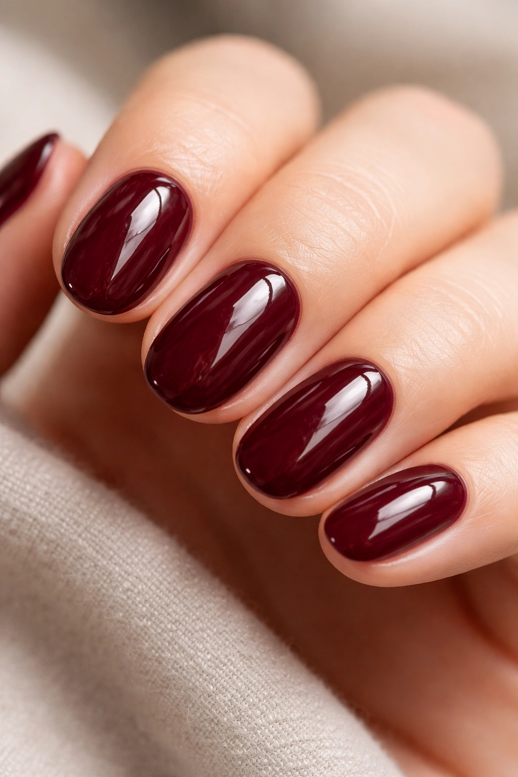 Close-up of burgundy wine short oval nails with glossy top coat on a neutral background