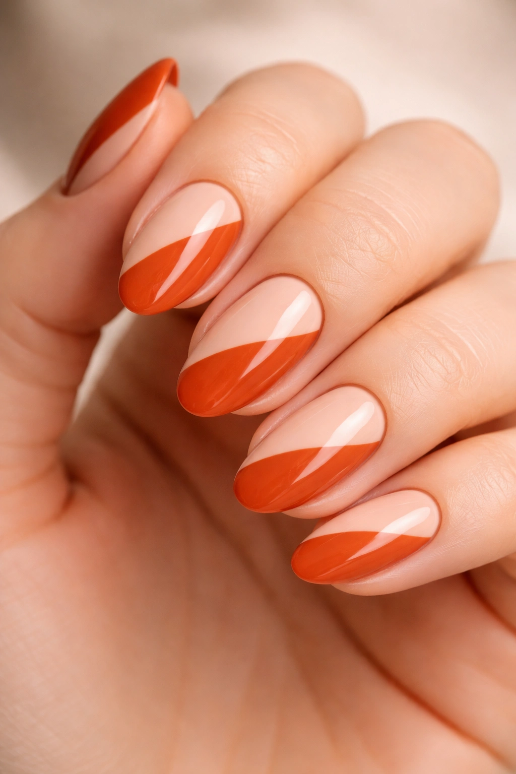 Close-up of burnt orange and nude color blocking on short almond nails with a clean diagonal split