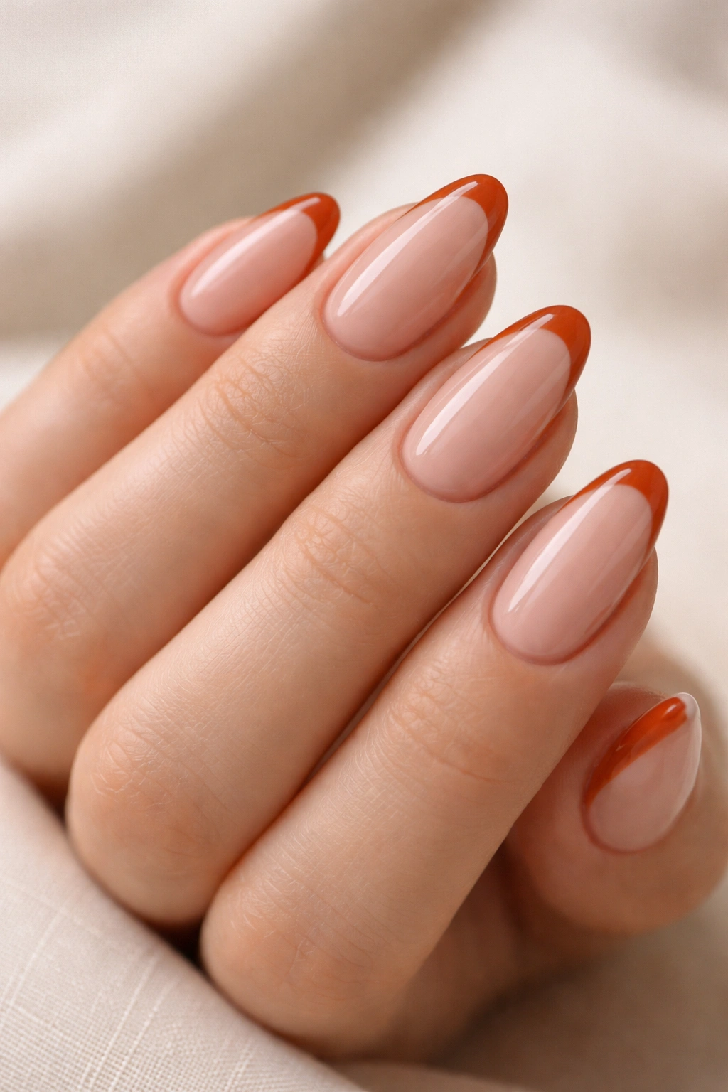 Nude almond nails with thin burnt orange French tips following the nail curve.