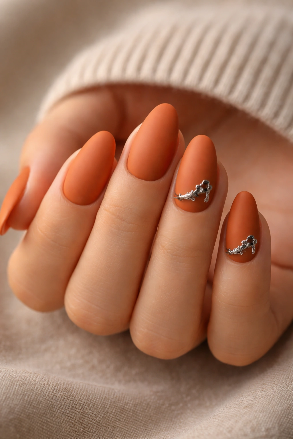Close-up of burnt orange short almond nails with tiny chrome spur accents on accent nails