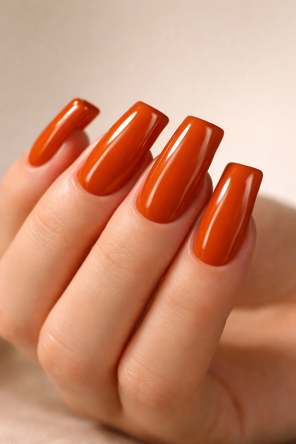 Close-up of glossy burnt orange duck nails on a neutral background