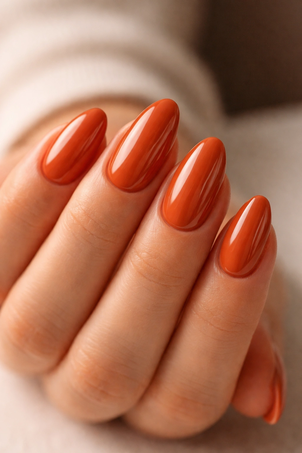 Close-up of short almond nails in glossy burnt orange with a curved almond shape.