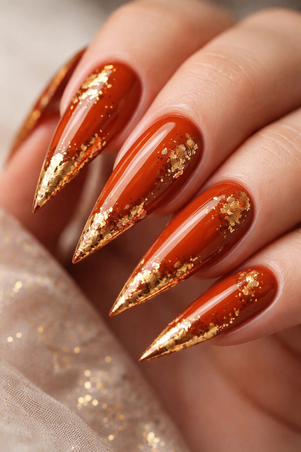 Close-up of burnt orange stiletto nails with gold leaf accents
