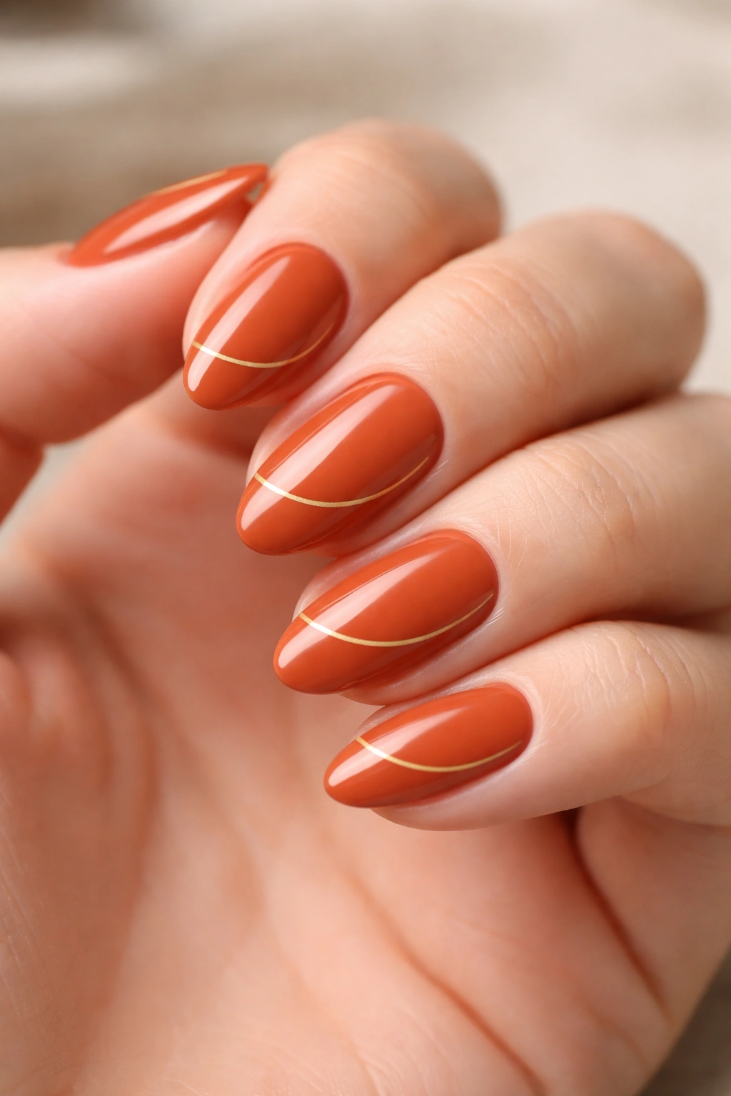 Close-up of burnt orange nails with minimal gold line art on almond nails