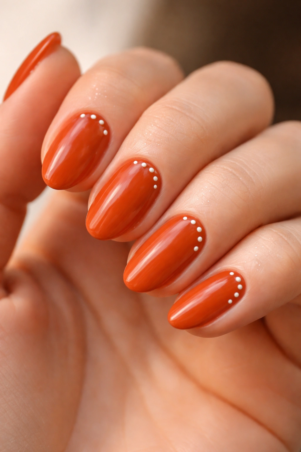 Close-up of burnt orange nails with tiny white dot art on short almond nails