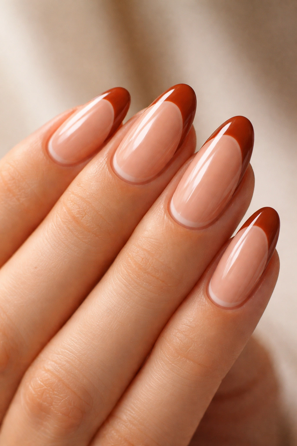 Close-up of medium-length almond nails with burnt sienna French tips and a 1mm negative space gap.