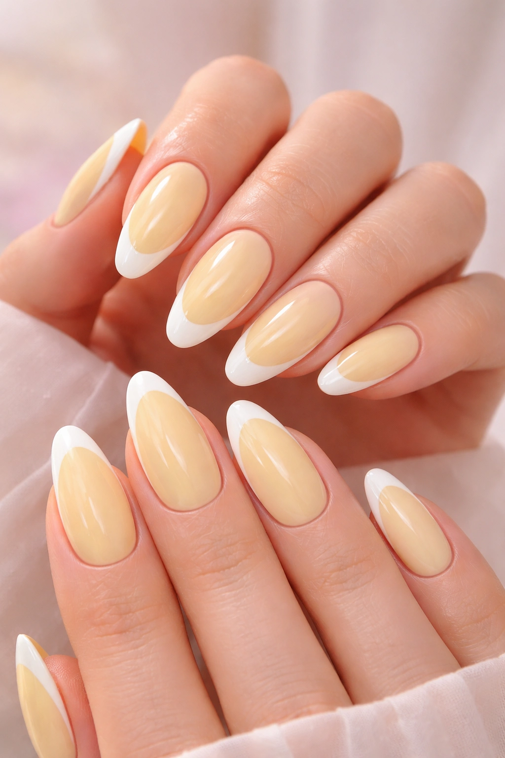 Close-up of butter yellow nails with white French tips on almond-shaped nails, studio lighting