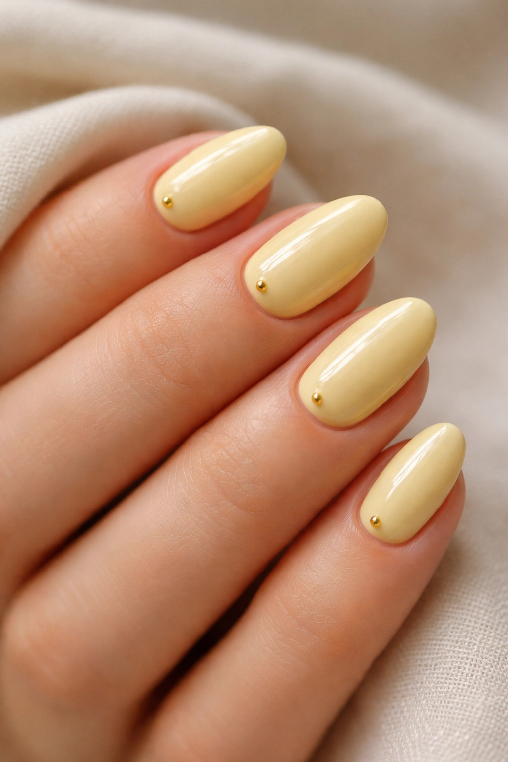 Butter yellow short almond nails with tiny gold studs near the cuticle