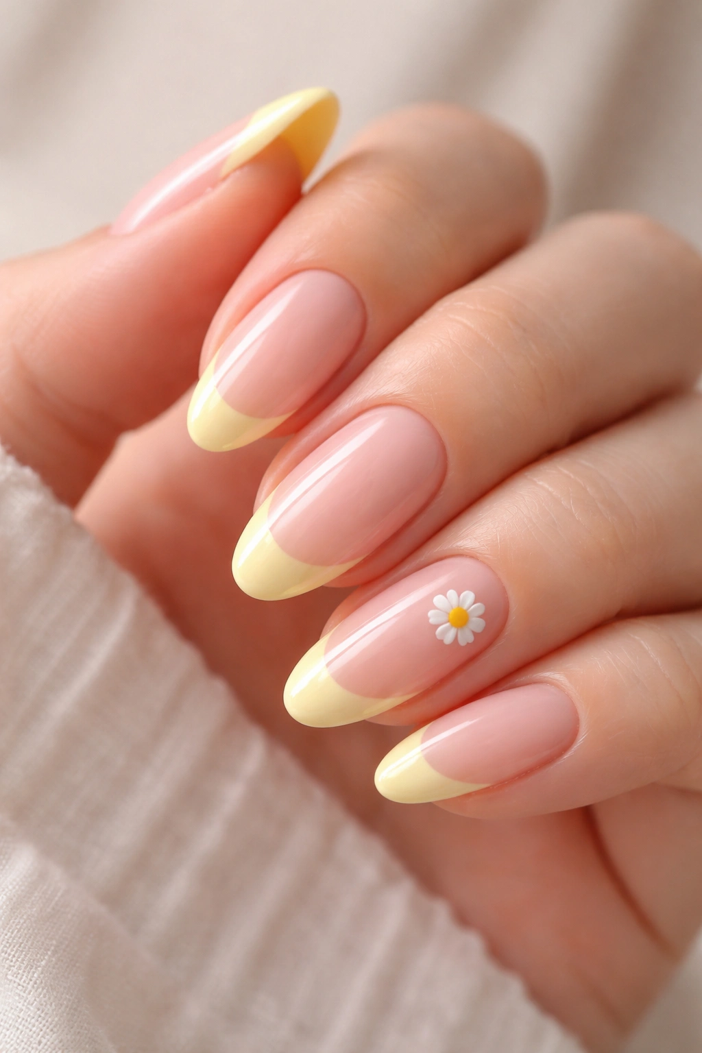 Close-up of natural pink nails with butter yellow tips and a daisy accent.