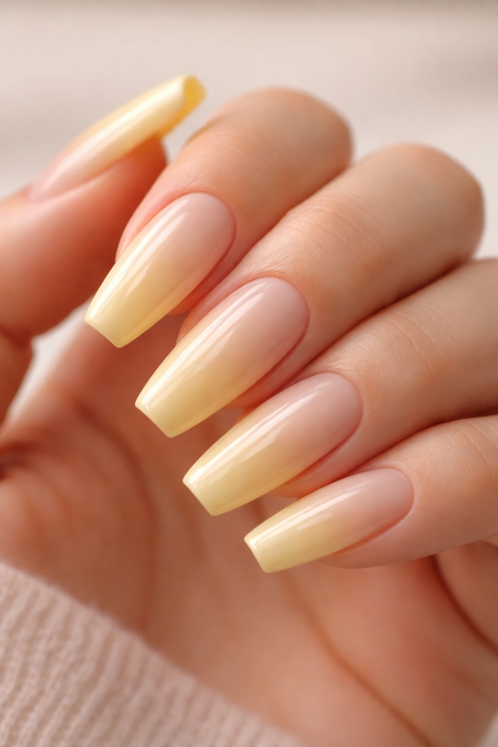 Close-up of buttercream yellow ballerina nails with sheer nude base and glossy finish