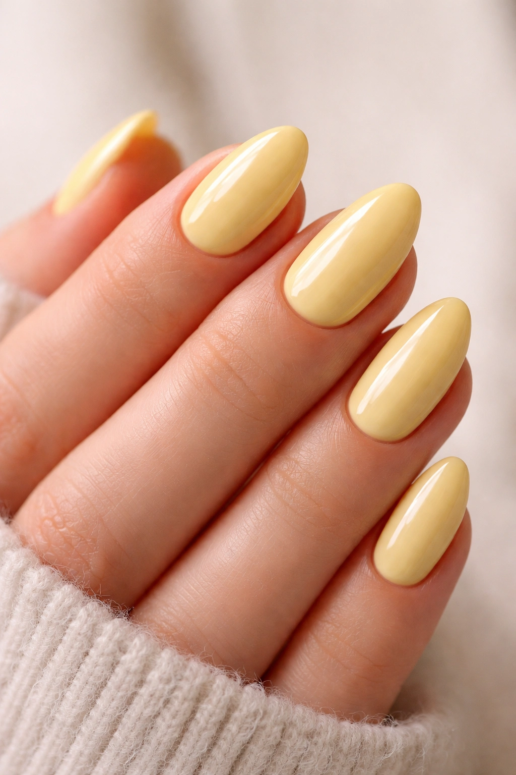 Close-up of short almond nails in buttercream yellow with glossy finish