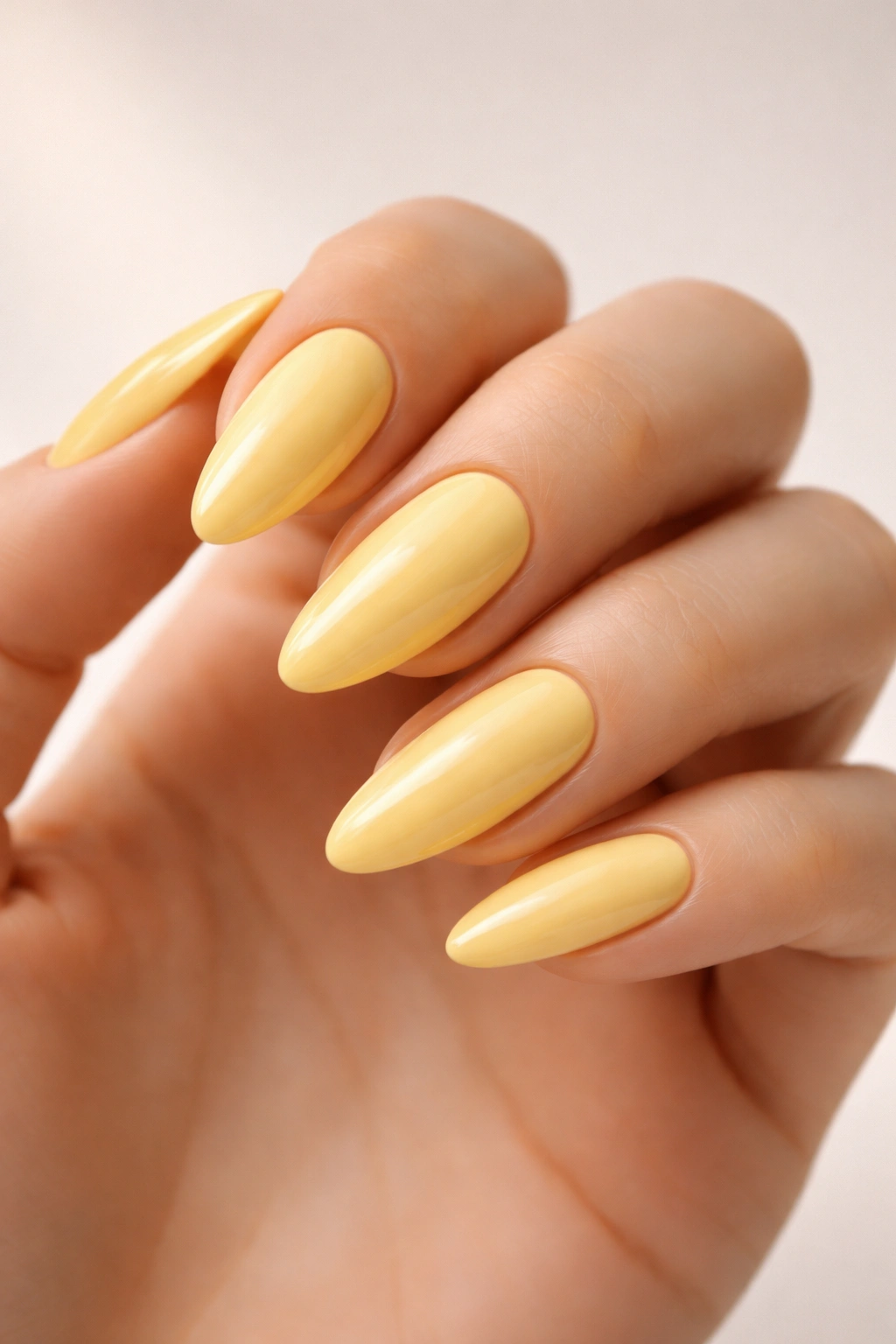 Close-up of almond-shaped buttercup yellow nails on a neutral background