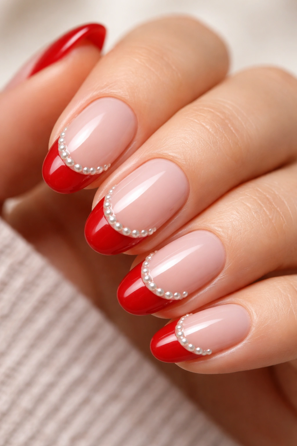 Close-up of a short almond nail with candy apple red tip and pearl accents along the smile line