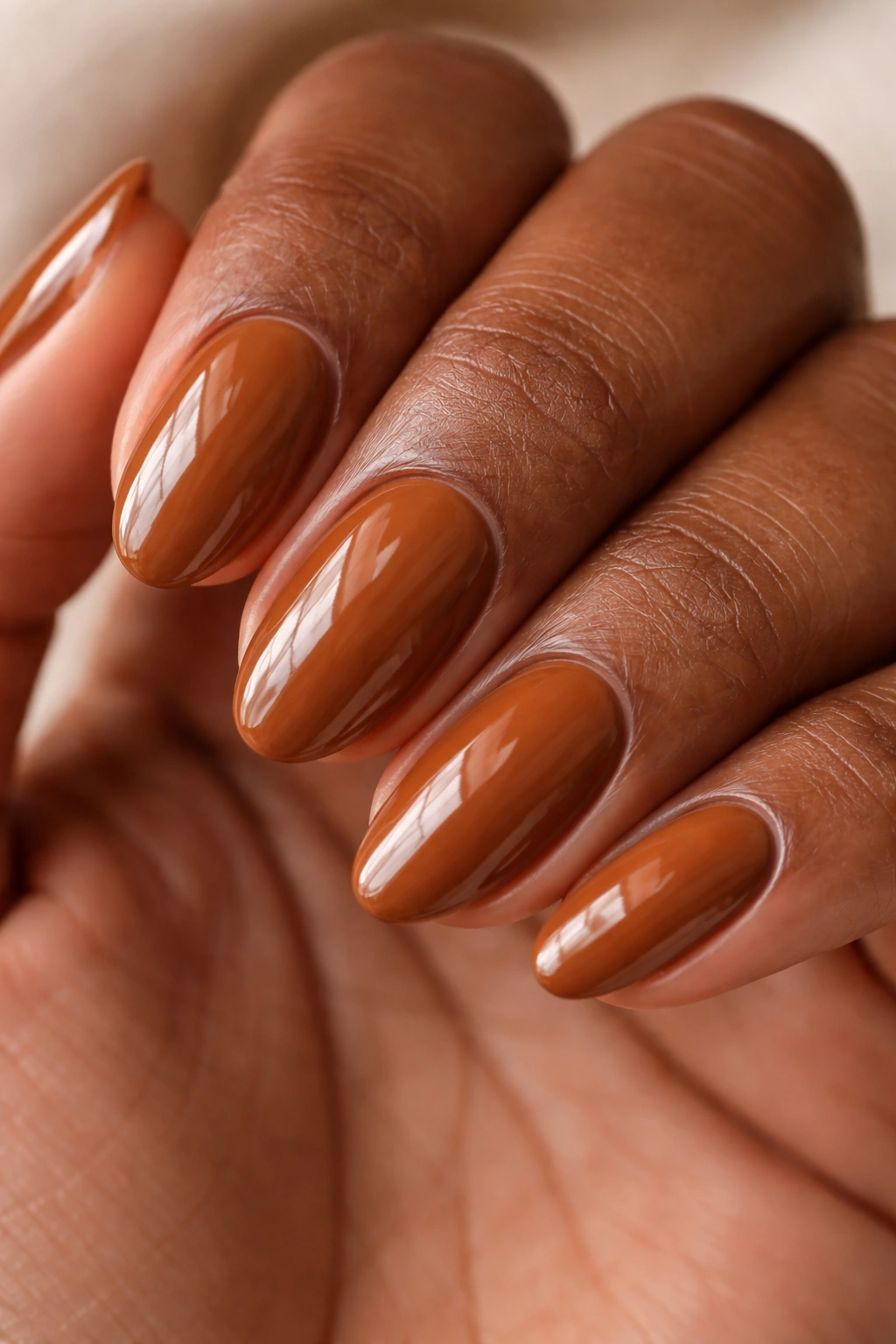 Close-up of short almond nails in caramel brown with glossy shine on dark skin