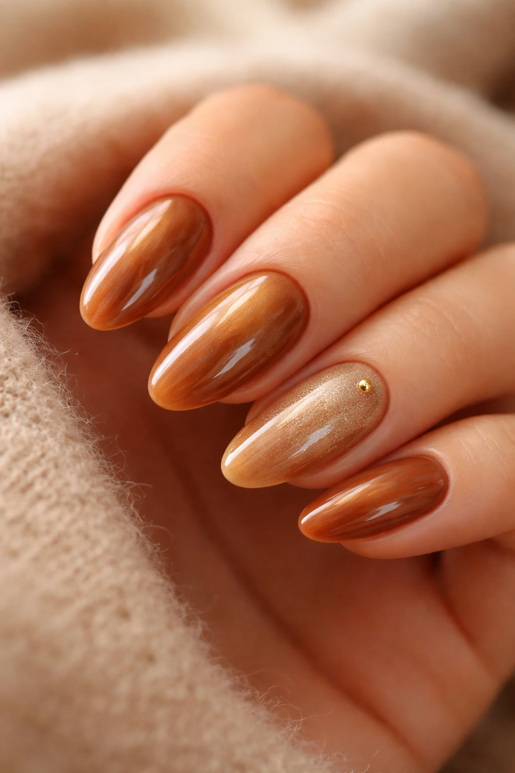 Glossy caramel latte nails with a gold accent on a soft neutral surface