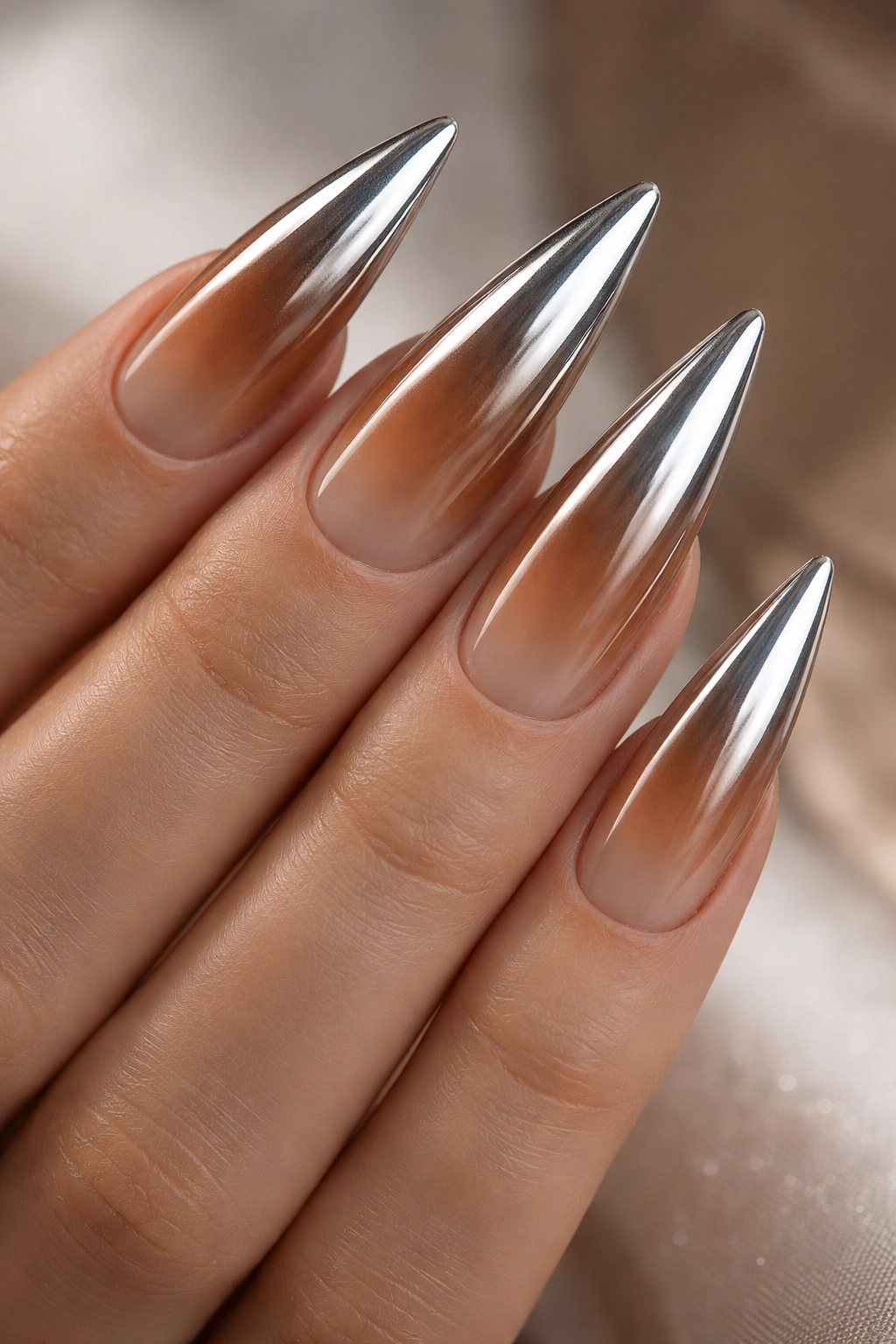 Close-up of caramel-to-nude ombre stiletto nails with chrome powder tips.
