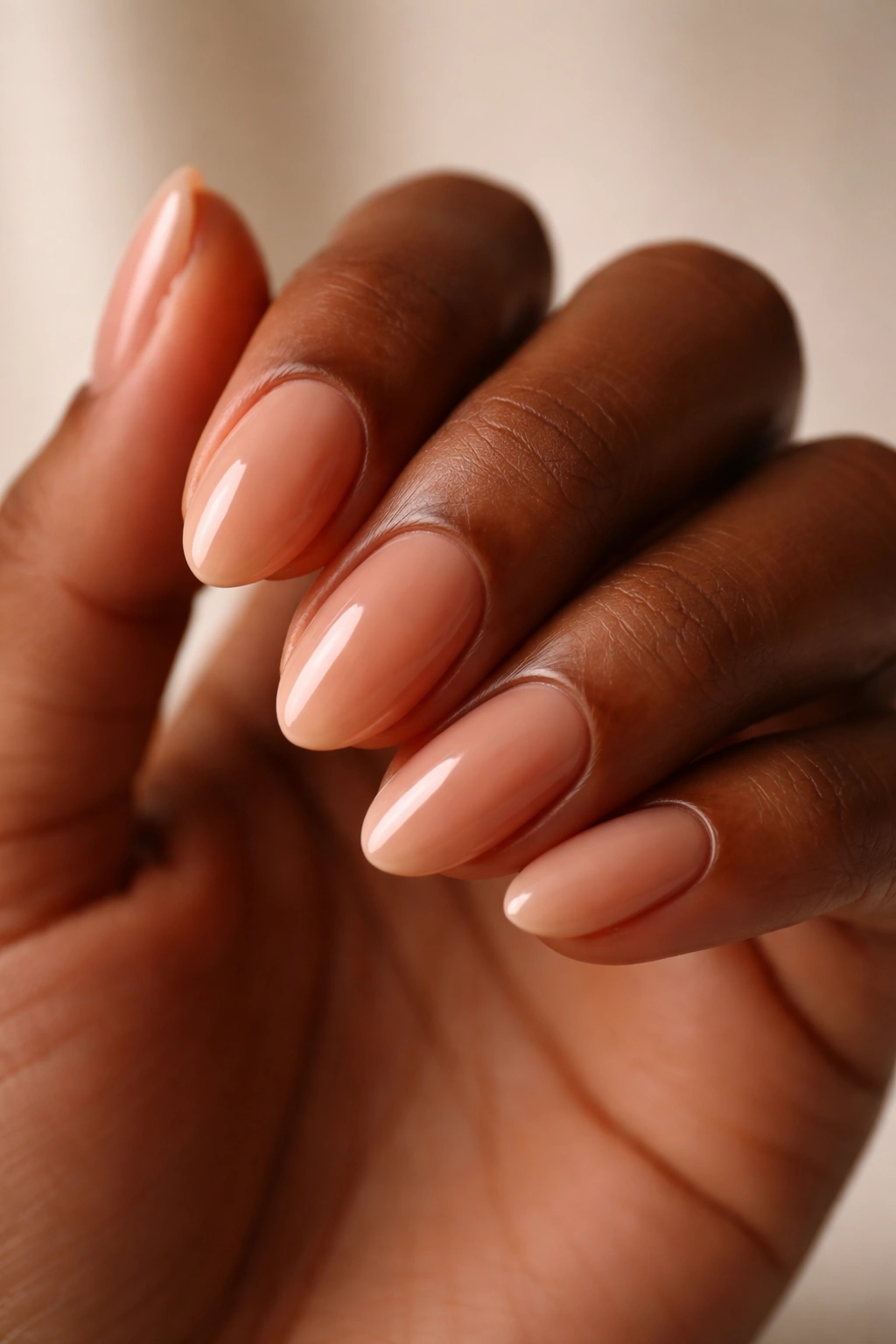 Close-up of a short almond nail on deeper skin with sheer caramel nude polish