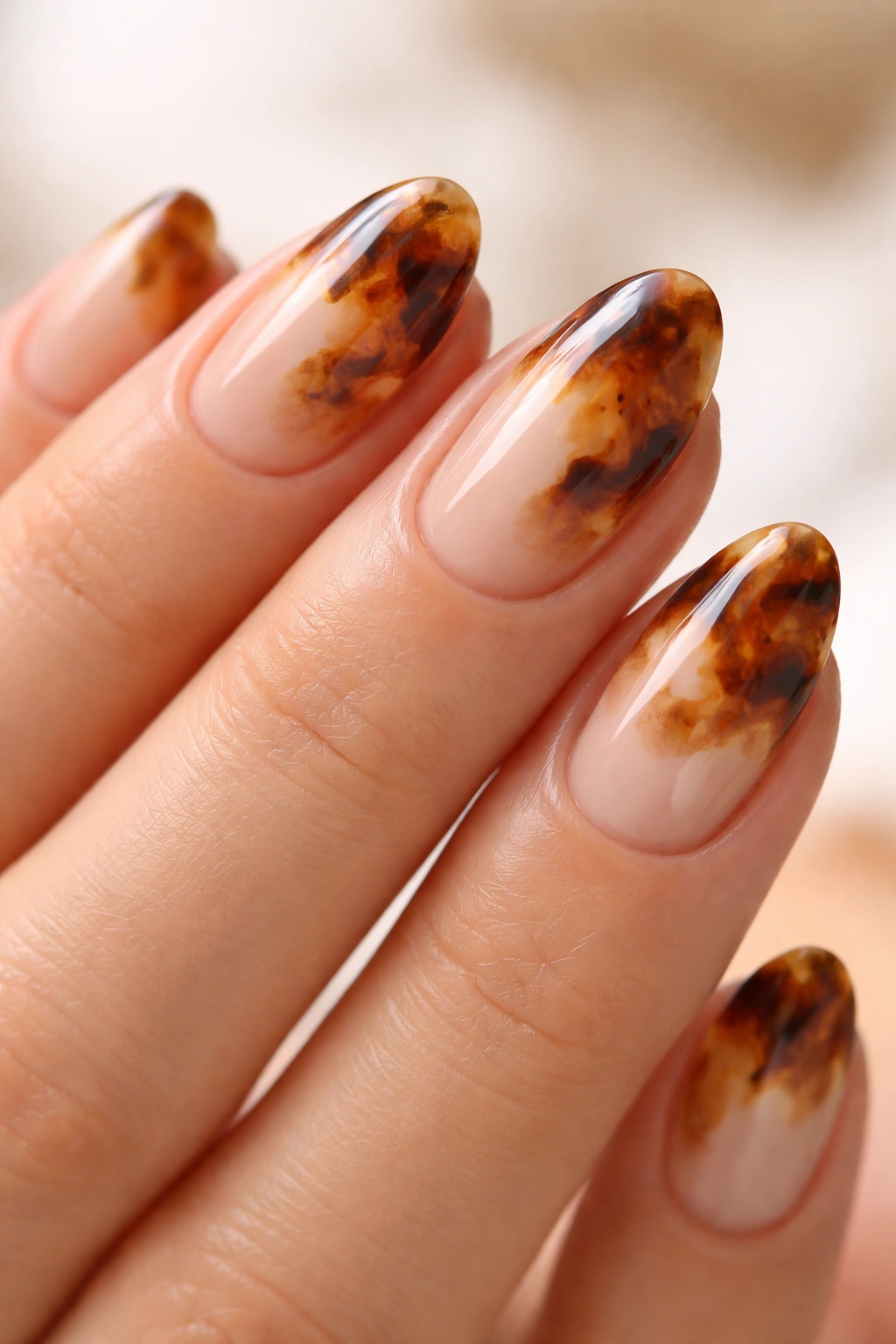 Close-up of short almond nails with caramel swirl tortoiseshell on milky nude base