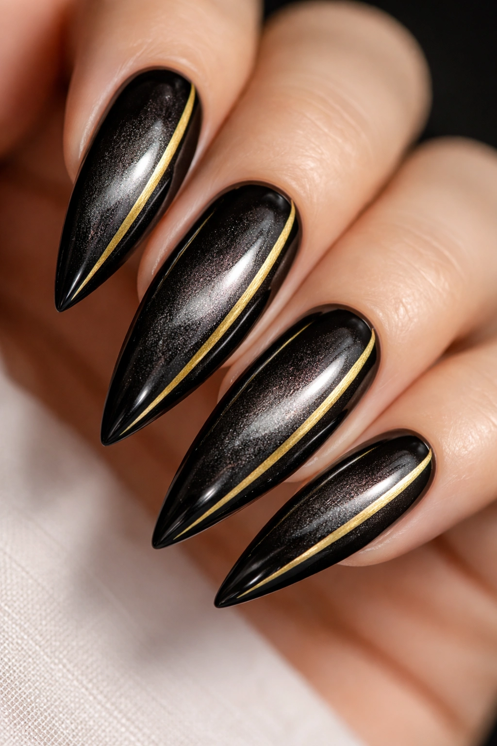 Black cat-eye stiletto nail with a gold accent stripe
