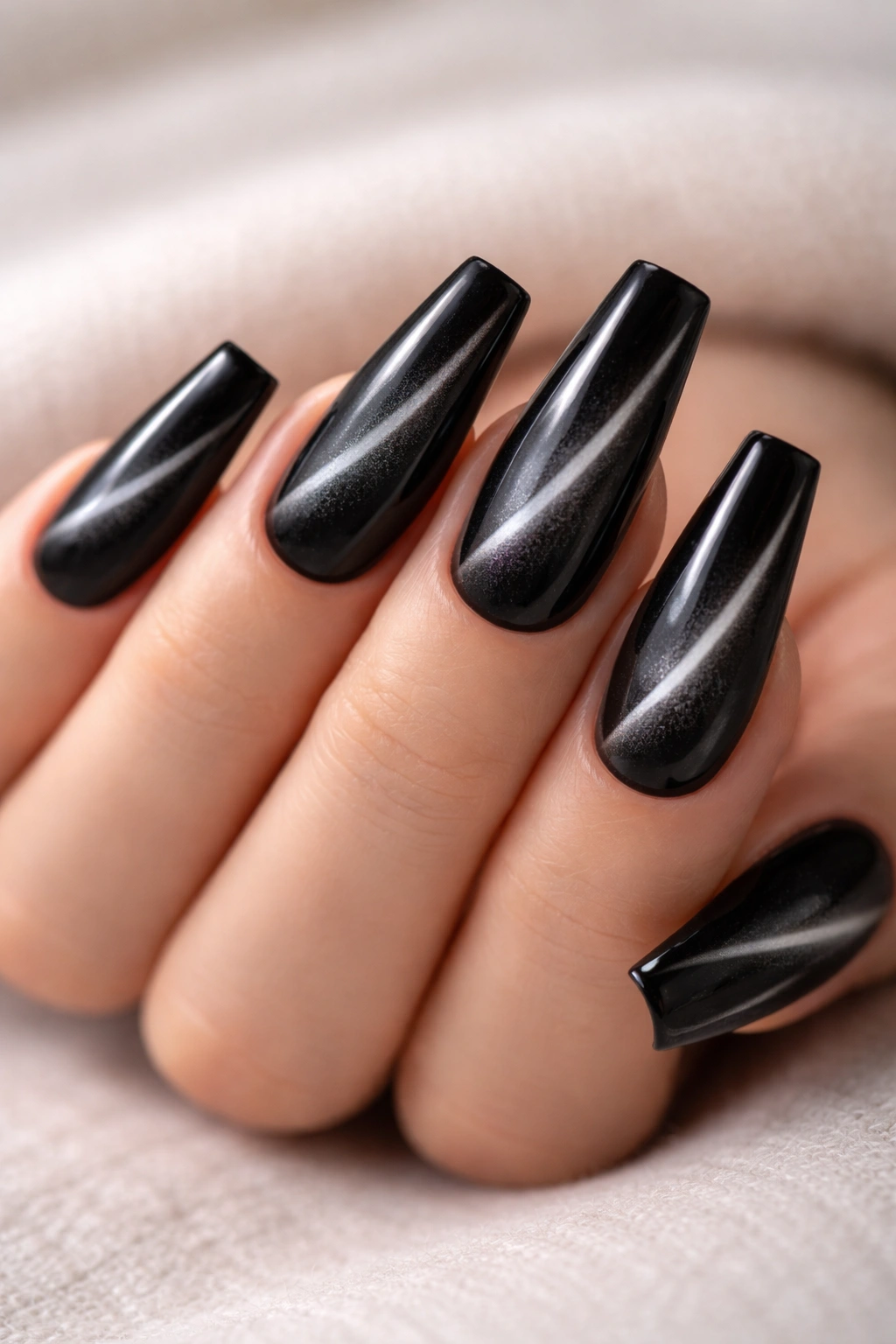 Close-up of black cat eye ballerina nails with a velvet stripe on a neutral background