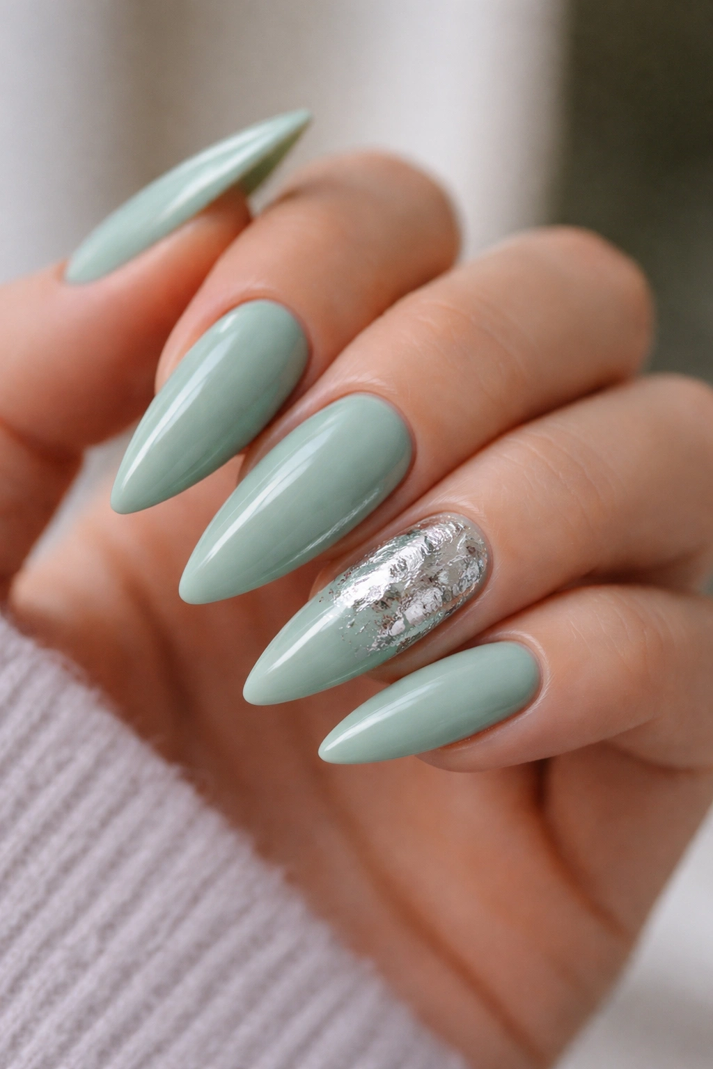 Close-up of celadon green nails with a single silver-leaf accent nail