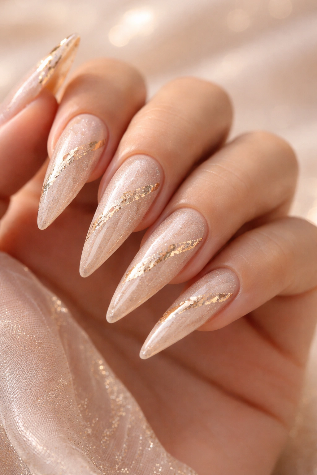 Close-up of champagne shimmer stiletto nails with gold foil accents