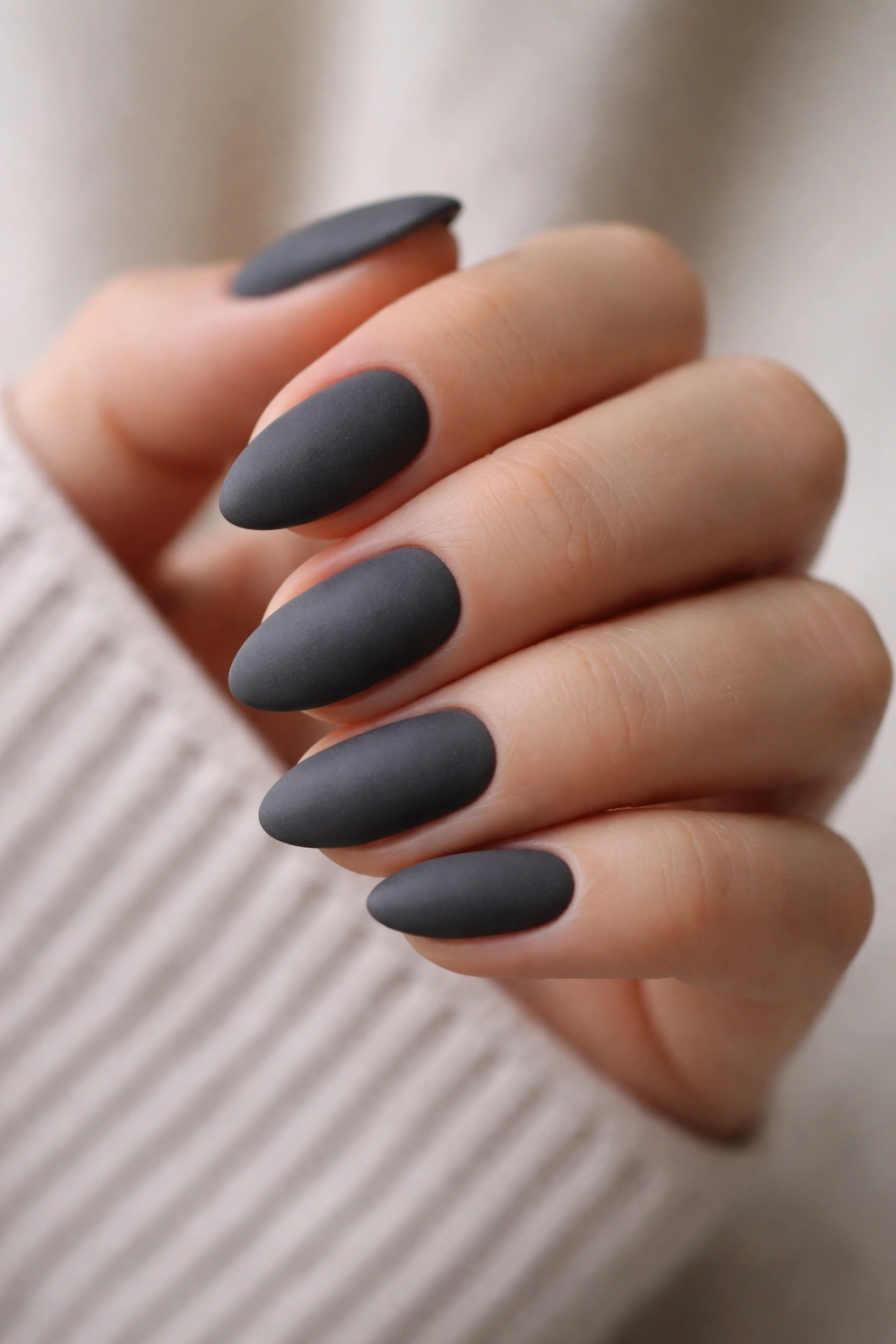 Close-up of matte charcoal almond nails on a hand