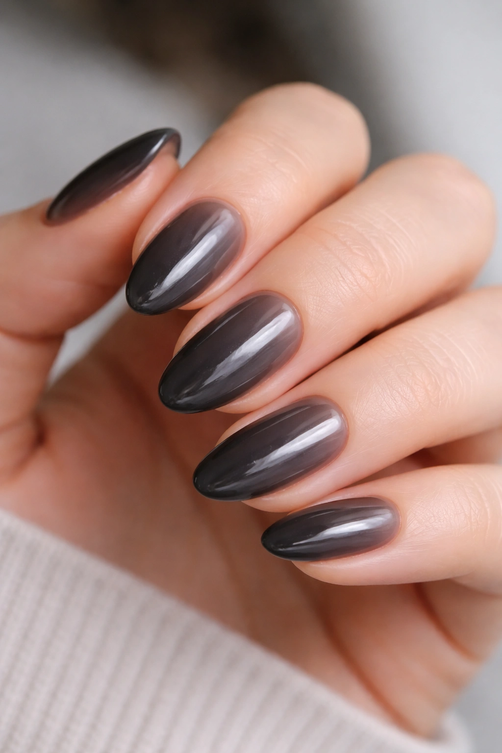 Close-up of short almond nails with sheer charcoal polish on a pale hand, translucent smoky gray.