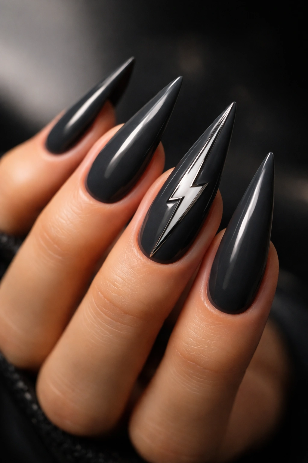 Close-up of charcoal gray stiletto nails with a metallic bolt design on a neutral background
