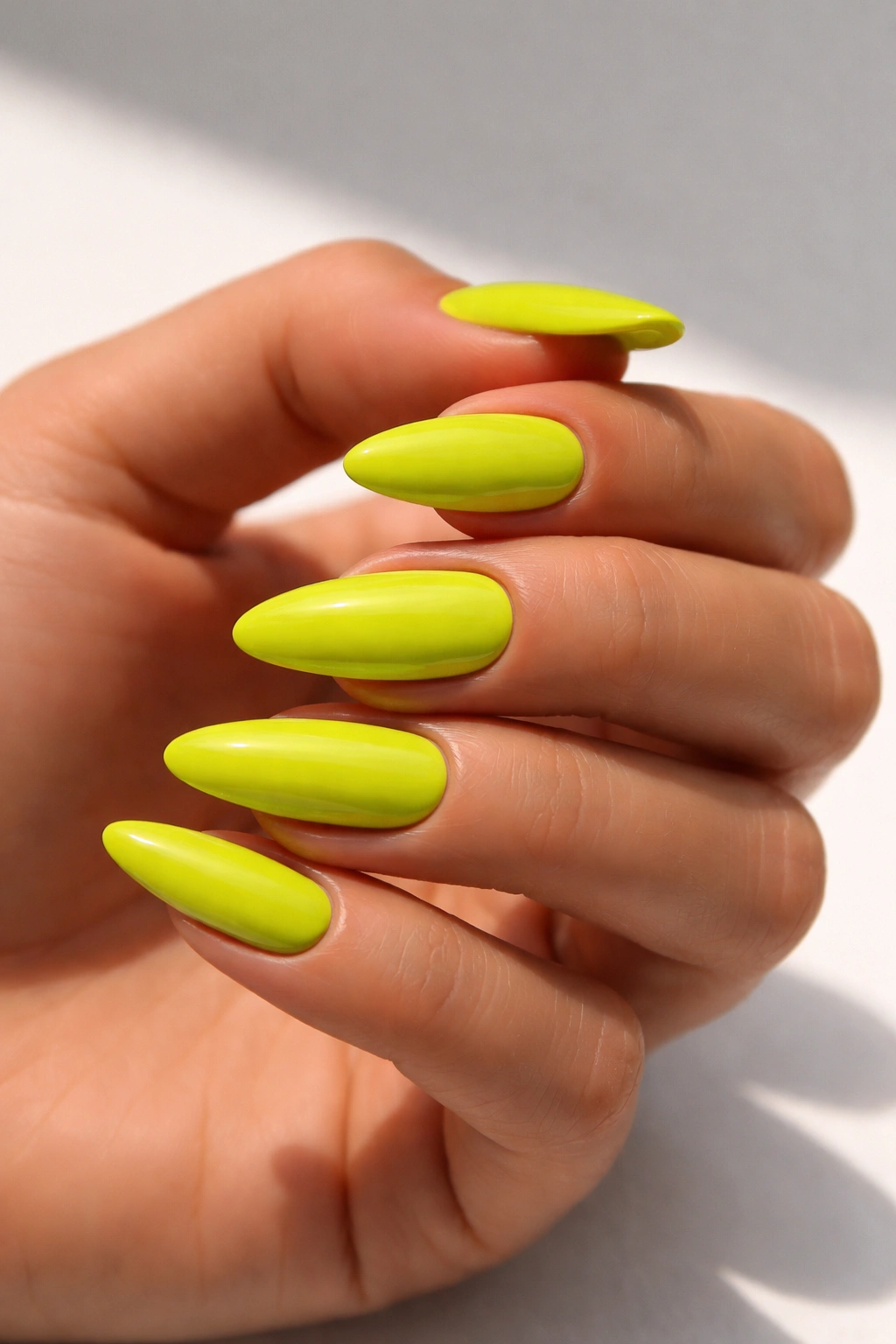 Close-up of chartreuse nails on sun-kissed skin with neutral background.