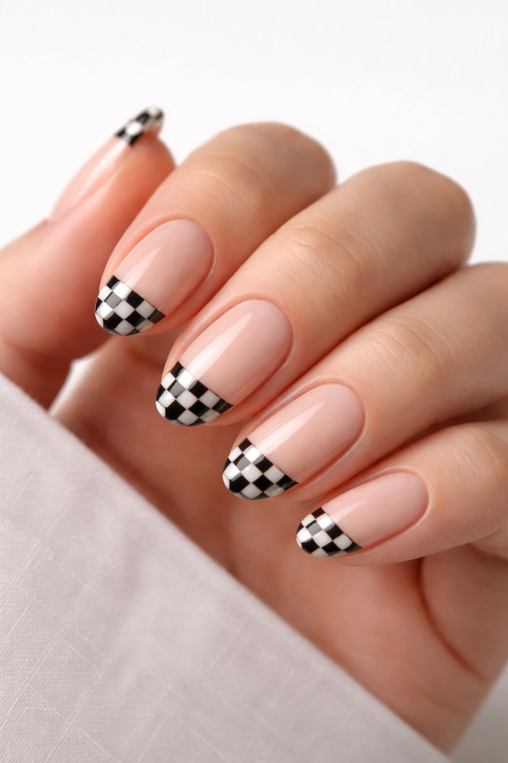 Close-up of short almond nails with tiny checkerboard tips on a nude base
