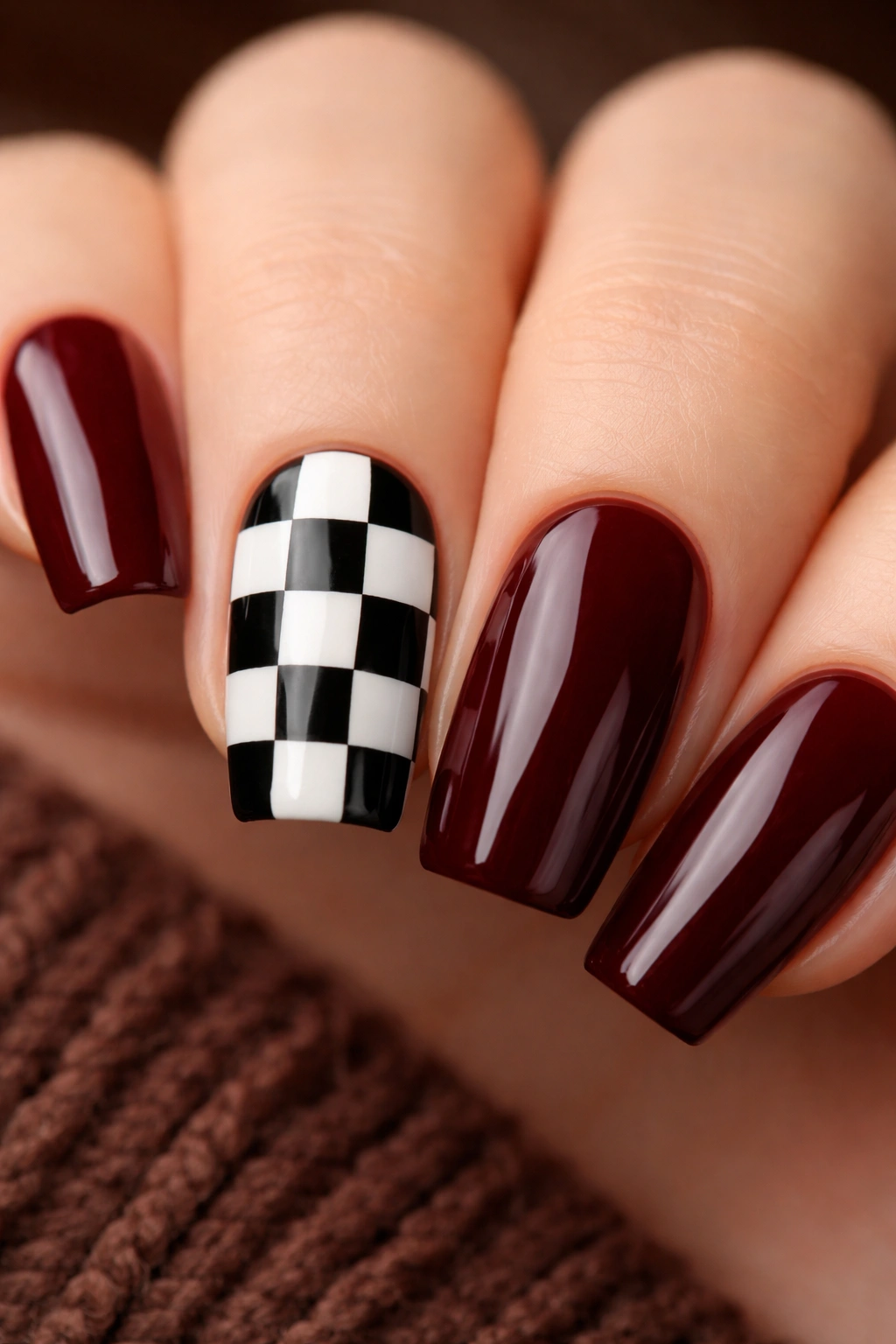 Close-up burgundy nail with black-and-white checkered accent nail.