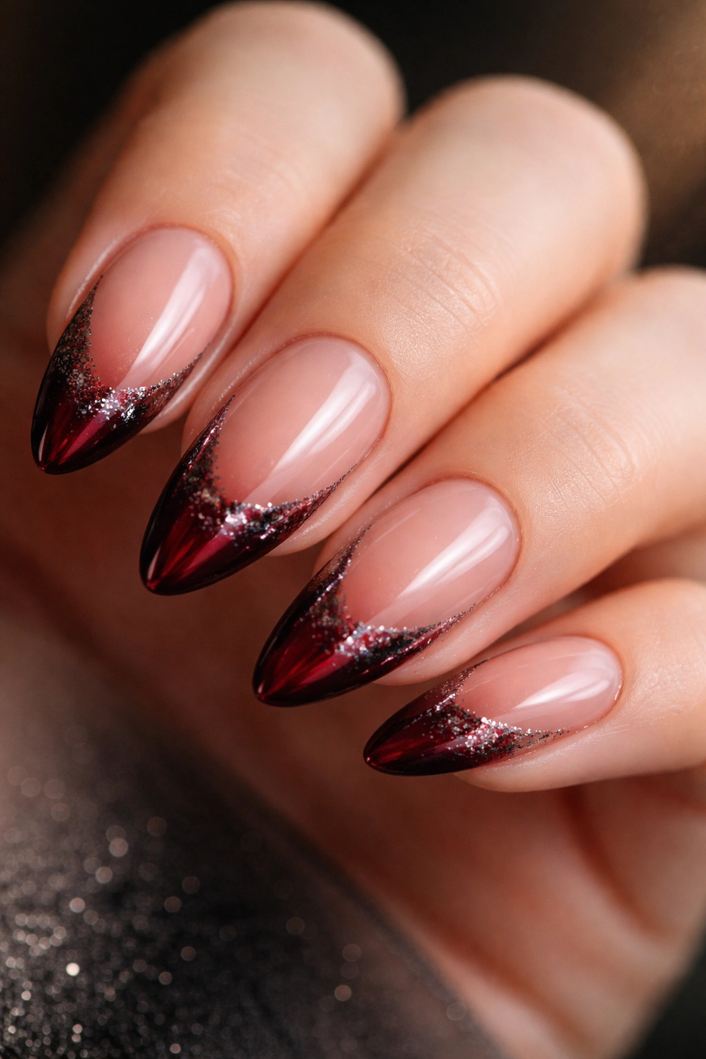 Close-up of almond nails with cherry cola red tips and smoky glitter for moody look