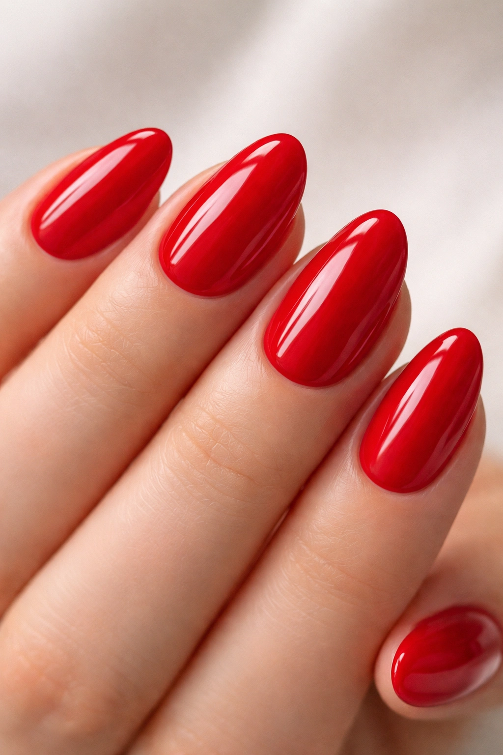 Close-up of short almond nails in cherry red with a tidy almond tip and glossy finish