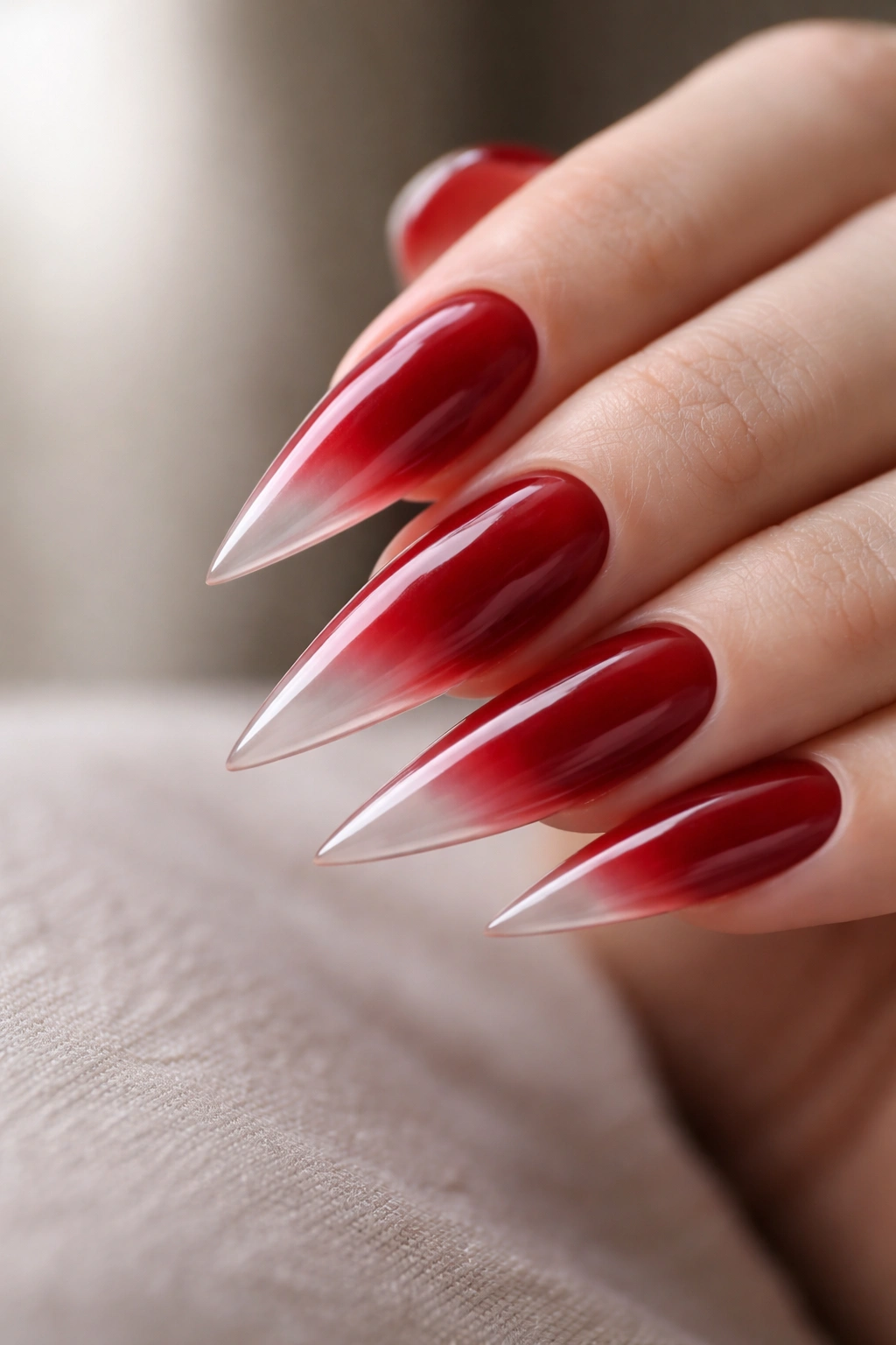 Close-up of cherry red stiletto nails with translucent tips gradient